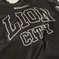 A black athletic jersey with 'LION CITY' printed in large white varsity-style block letters across the front, with 'MAZZIVEKLO' above it and a number 65 visible on the shoulder.